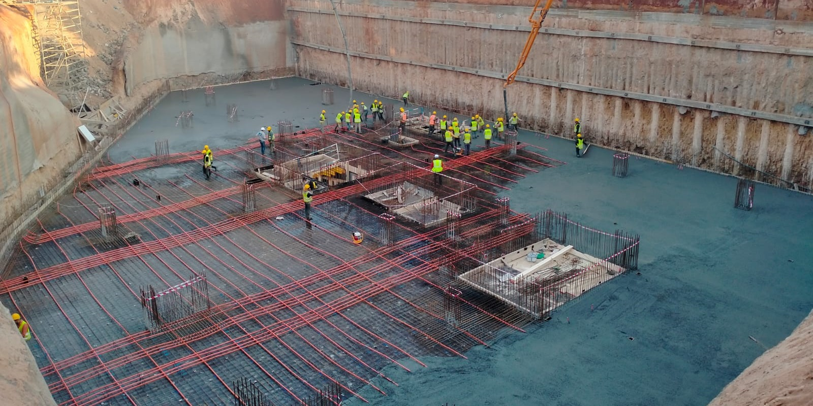 Large scale construction site showing workers pouring concrete over a post tension slab foundation grid with visible unbonded tendons.